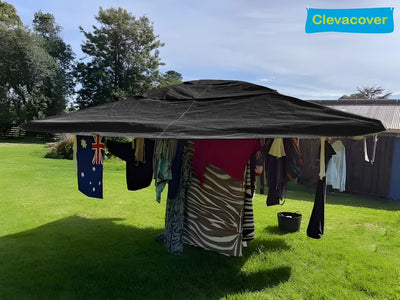 Outdoor setting with a large black canopy covering clothes on a grassy area, featuring the Clevacover brand.